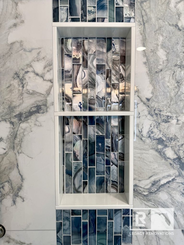 Built-in two-shelf shower niche with blue agate glass accent mosaic tiles surrounded by marble-look wall tile in a Jacksonville, FL bathroom.