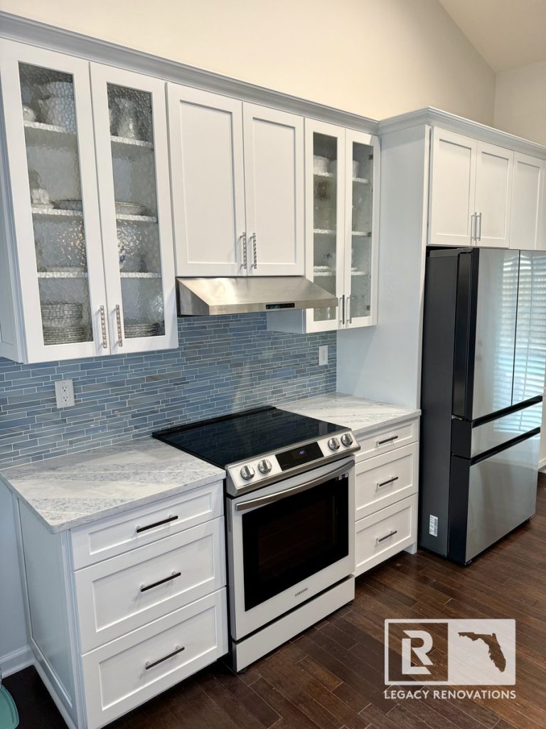 Remodeled kitchen with full-height cabinetry, glass display cabinets, quartz countertops, stainless steel refrigerator, electric range, vent hood, and blue glass tile backsplash in Jacksonville, FL.