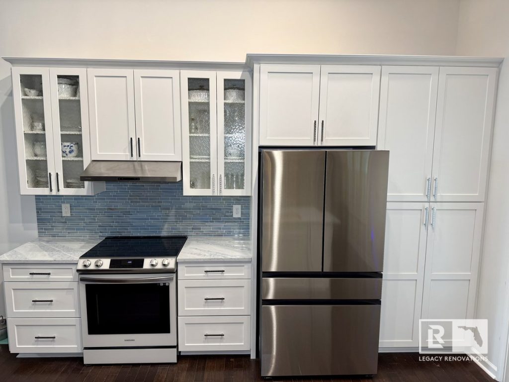 Kitchen remodel with full-height white shaker cabinets, French door refrigerator, stainless steel range and vent hood, blue glass subway tile backsplash, and marble-look countertops in Jacksonville, FL.