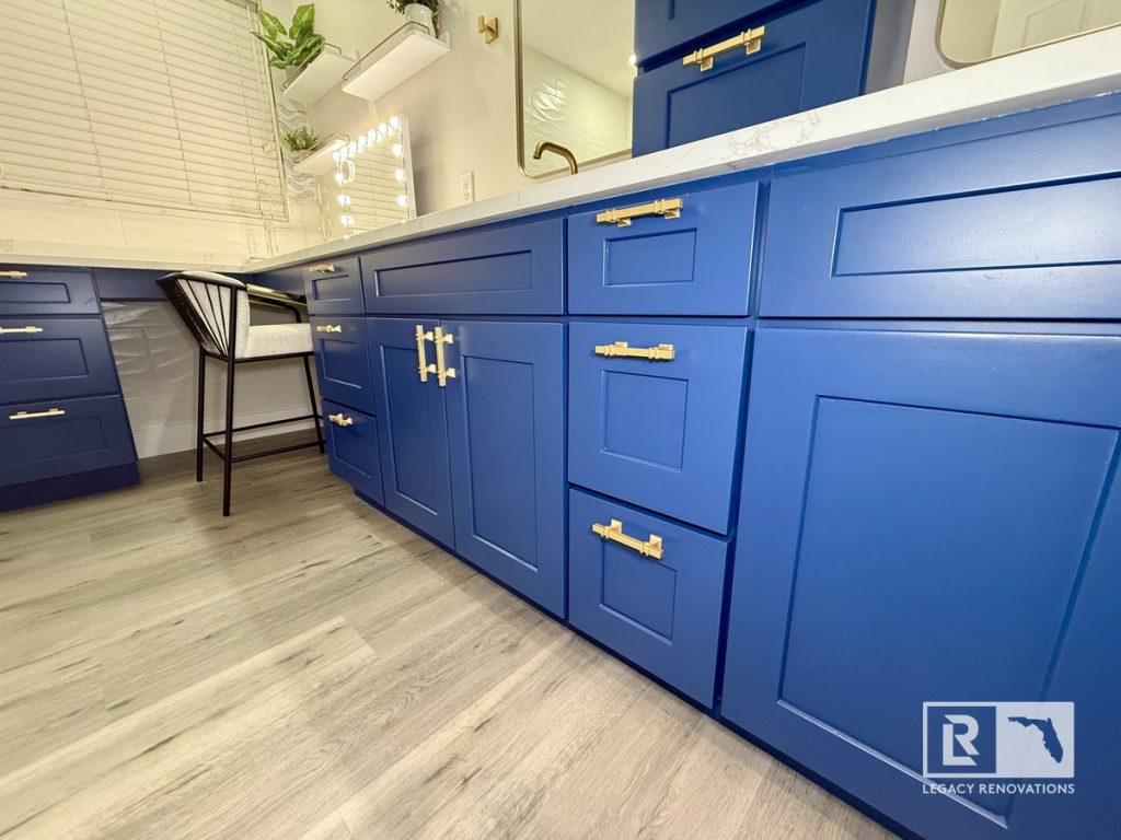 Custom navy blue shaker bathroom cabinets with brushed brass hardware, white quartz countertop, and luxury vinyl plank flooring in a Jacksonville, Florida bathroom remodel.