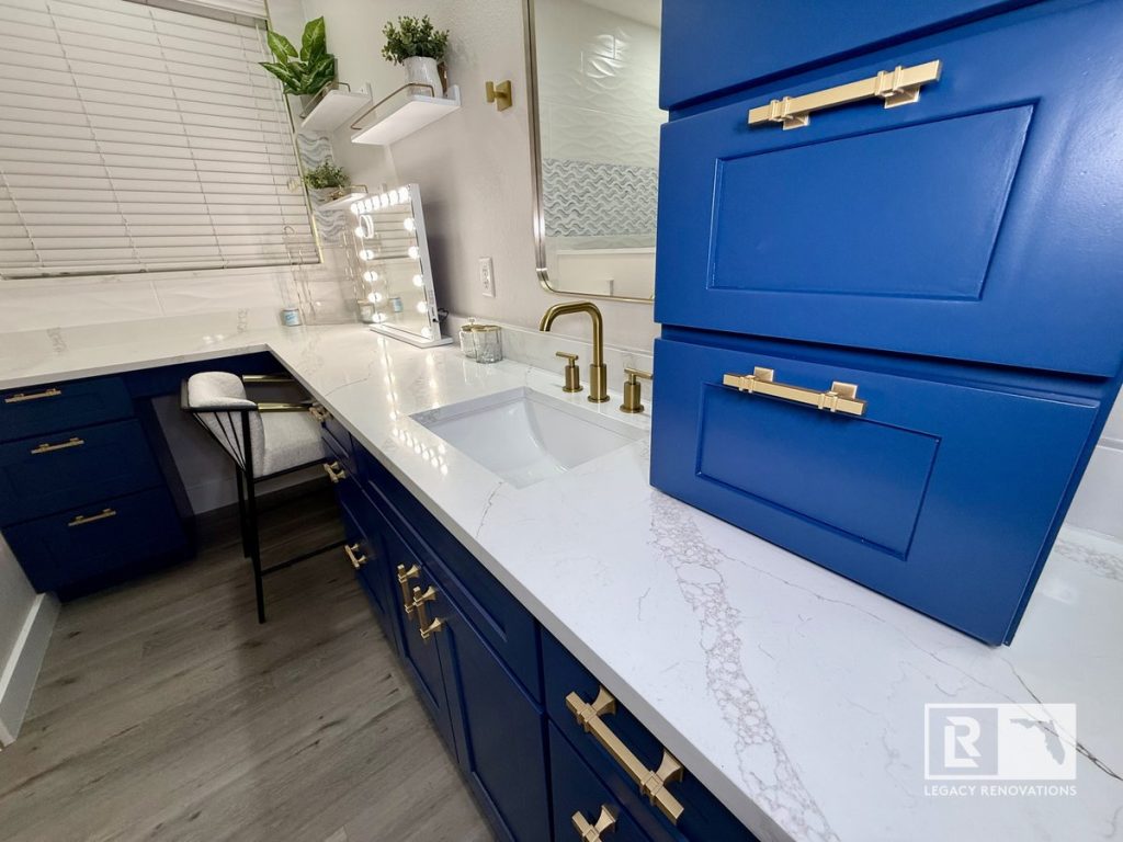 Custom navy blue bathroom vanity with a white quartz countertop, brushed brass faucet, and built-in makeup station in a Jacksonville, Florida bathroom remodel.