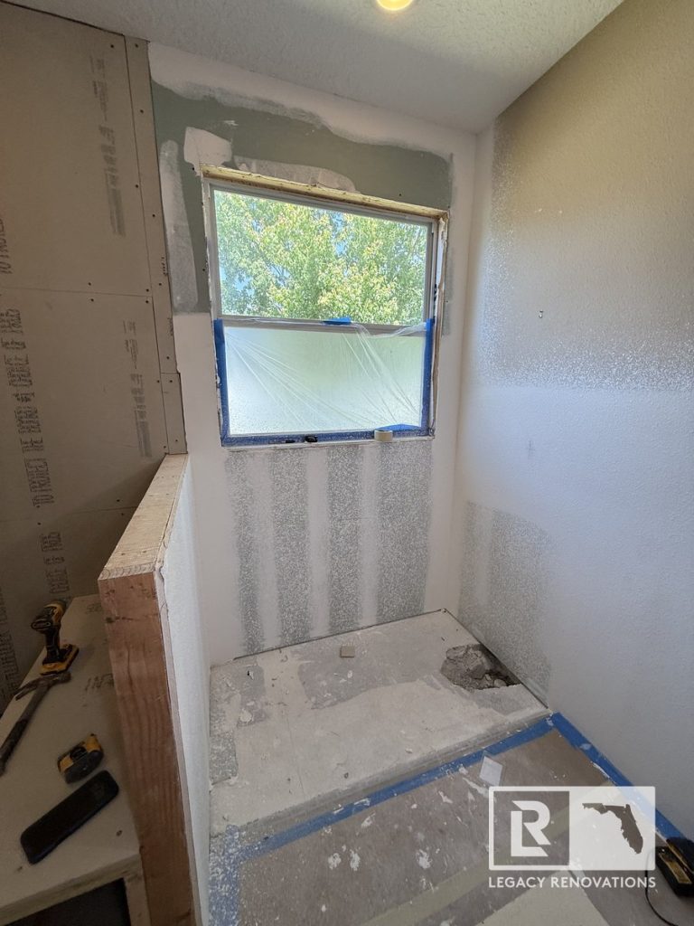 Bathroom remodel in progress in Jacksonville, Florida showing a newly installed shower base, framed half wall, drywall finishing around the shower area, recessed lighting, and preparation for tile installation.