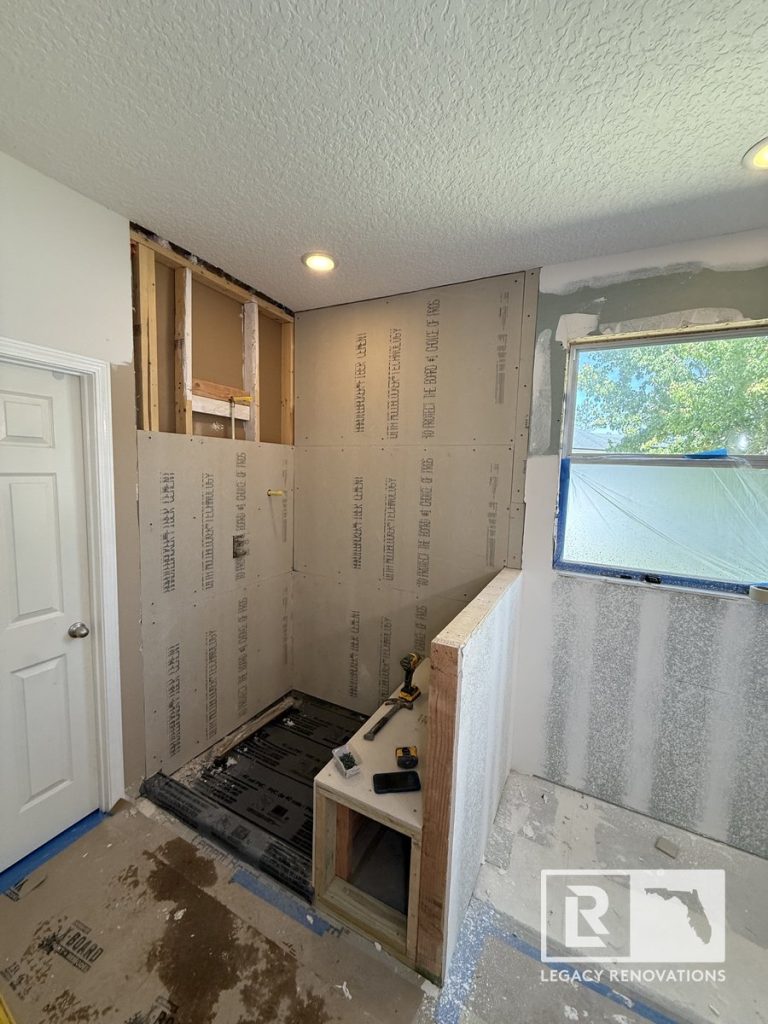 Bathroom remodel in progress in Jacksonville, Florida showing walk-in shower framing, cement backer board walls, built-in shower bench, recessed lighting, and preparation for waterproofing and tile installation.