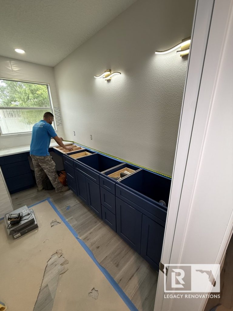 Bathroom remodel in progress in Jacksonville, Florida showing navy blue vanity cabinet installation, updated flooring, modern wall lighting, and ongoing renovation work.