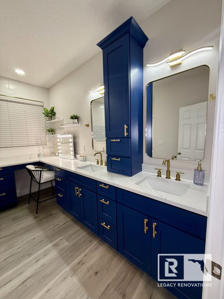 Custom navy-blue double vanity in a Jacksonville FL bathroom remodel featuring quartz countertops, gold fixtures, modern mirrors, and a built-in makeup vanity.