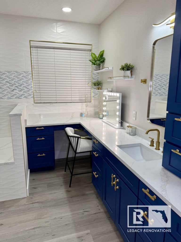 Luxury bathroom remodel in Jacksonville, Florida featuring a custom navy blue vanity, white quartz countertops, brushed gold fixtures, built-in makeup station, decorative accent tile, and modern storage cabinetry.