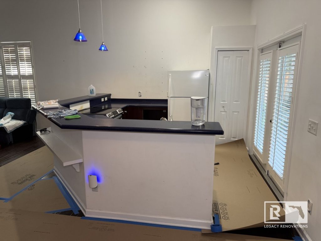 Before kitchen renovation showing a raised serving bar, blue countertops, pendant lights, white refrigerator, tall ceilings, and patio doors in a Jacksonville, Florida home.