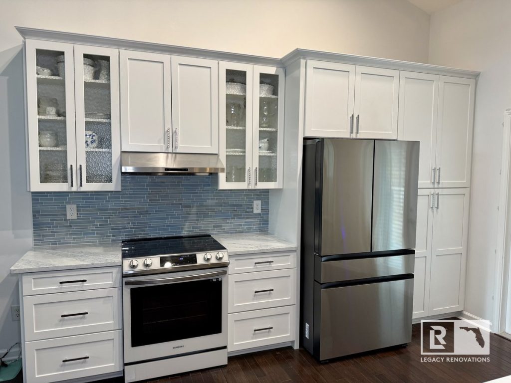 Modern Jacksonville kitchen remodel featuring white shaker cabinets, gray countertops, blue glass tile backsplash, stainless steel appliances, and tall pantry storage.