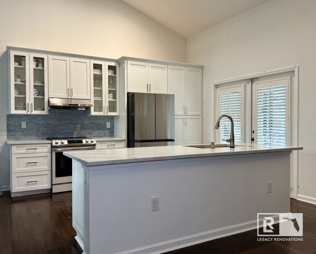Open-concept kitchen remodel featuring a large quartz island, ceiling-height cabinets, stainless steel appliances, blue glass tile backsplash, pull-down kitchen faucet, and patio doors in Jacksonville, FL.