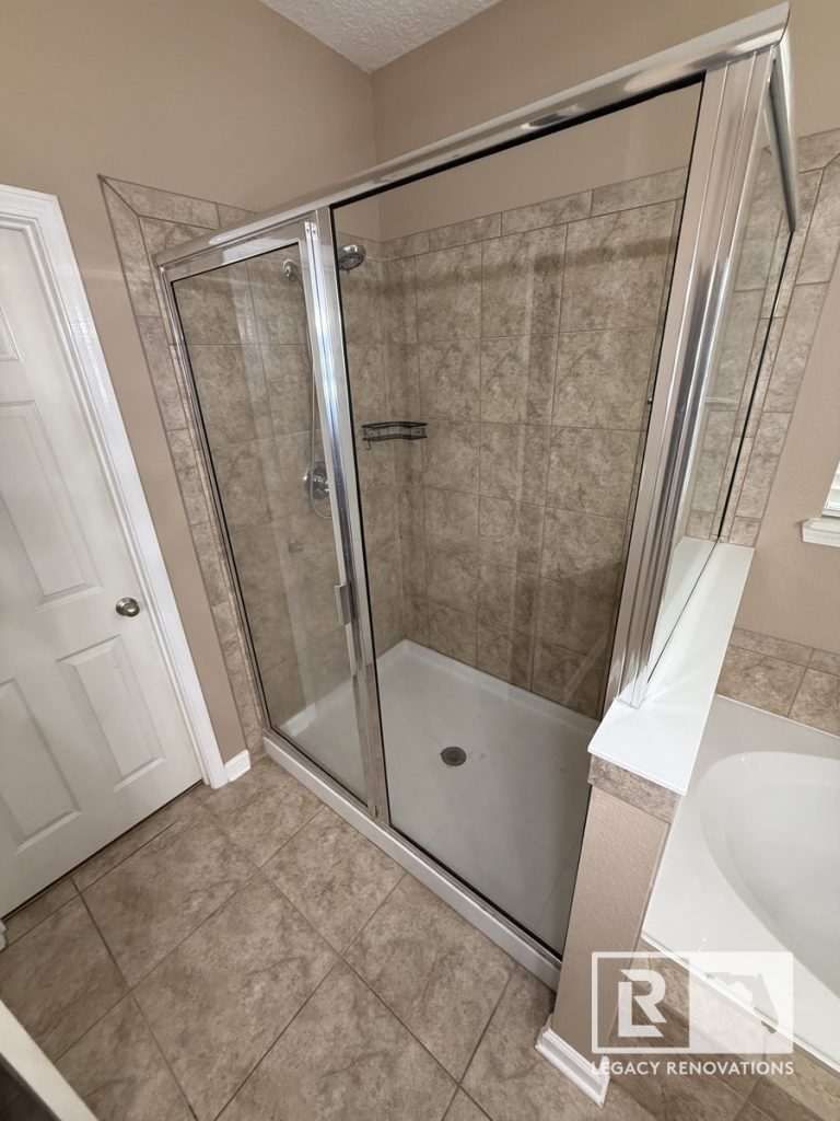 Corner view of the original walk-in shower in Jacksonville, Florida showing a framed sliding glass enclosure, ceramic tile walls, shower fixtures, and the pre-remodel bathroom configuration.