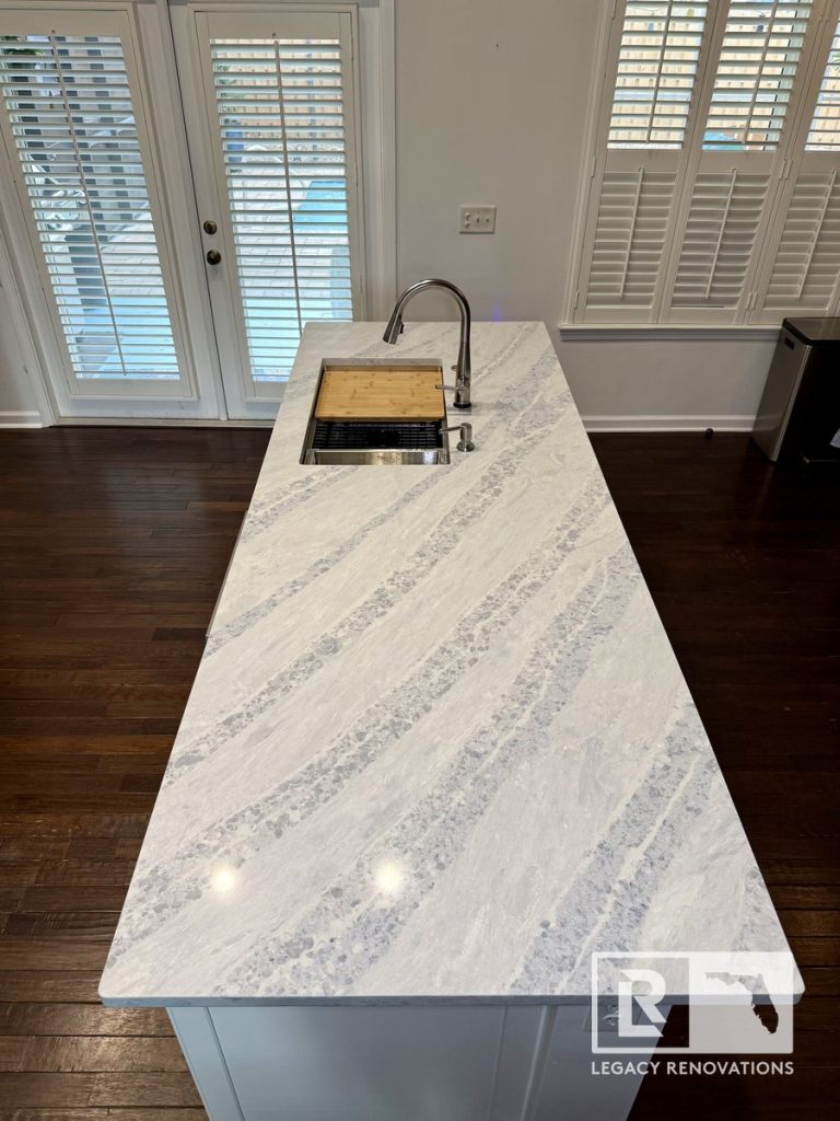 Large kitchen island with a gray-veined quartz countertop, workstation undermount sink, pull-down faucet, integrated cutting board, and open-concept layout in Jacksonville, FL.