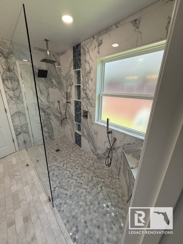 Spacious luxury walk-in shower with frameless glass enclosure, marble wall tile, rain showerhead, mosaic floor tile, and built-in bench in Jacksonville, FL.