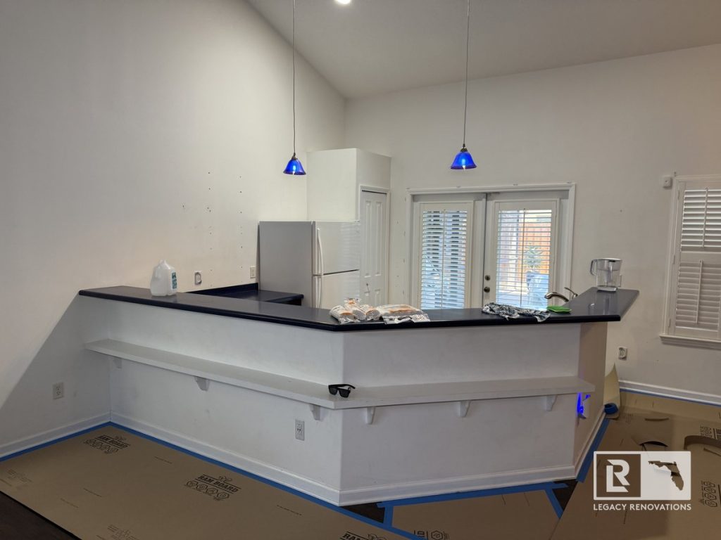 Kitchen before renovation featuring a wraparound peninsula with dark blue countertops, vaulted ceiling, pendant lights, patio doors, and an open floor plan in a Jacksonville, Florida home.