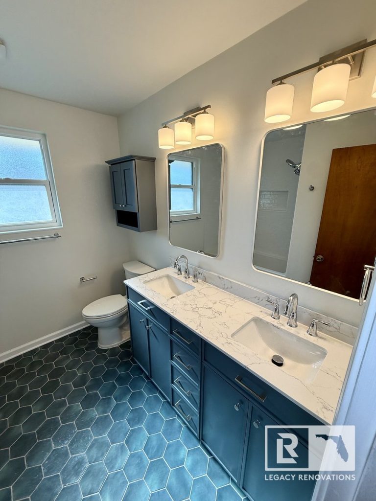 Modern bathroom remodel in Jacksonville, Florida featuring a double vanity with a quartz countertop, blue cabinets, hexagon floor tile, contemporary lighting, and brushed nickel fixtures.