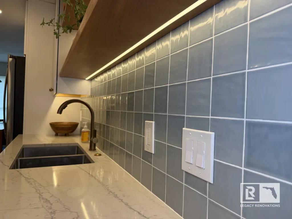 Angle view of glossy blue square backsplash tiles and white quartz countertops with under-shelf LED strip lighting in a Jacksonville, FL kitchen remodel.
