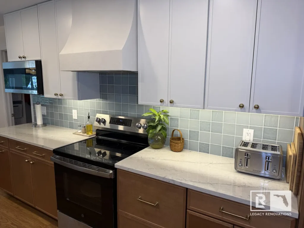 Contemporary kitchen featuring a custom plaster range hood, blue tile backsplash, white upper cabinets, quartz countertops, and stainless steel appliances.