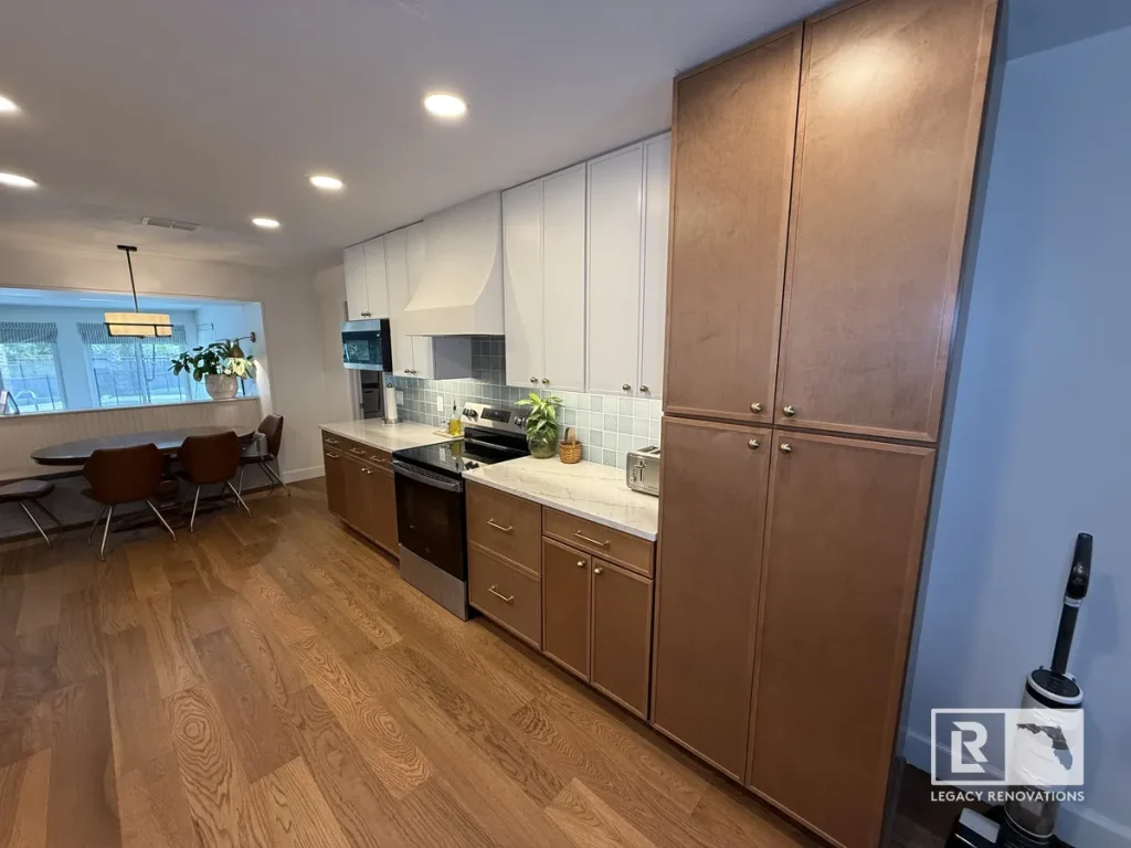 Wide-angle view of floor-to-ceiling natural wood pantry cabinets alongside two-tone kitchen cabinetry and hardwood floors in Jacksonville, FL.