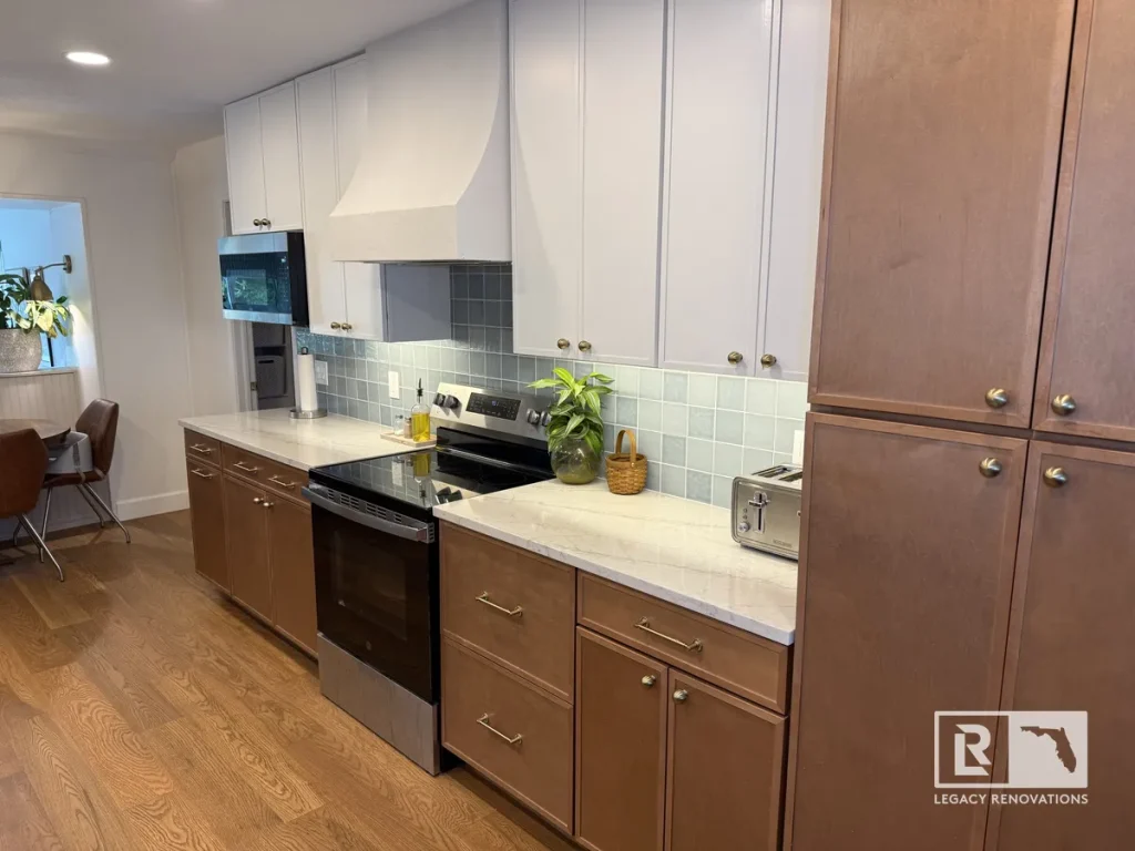 Modern two-tone kitchen featuring light grey upper cabinets, natural wood lower cabinetry, custom plaster range hood, and blue tile backsplash in Jacksonville, FL.