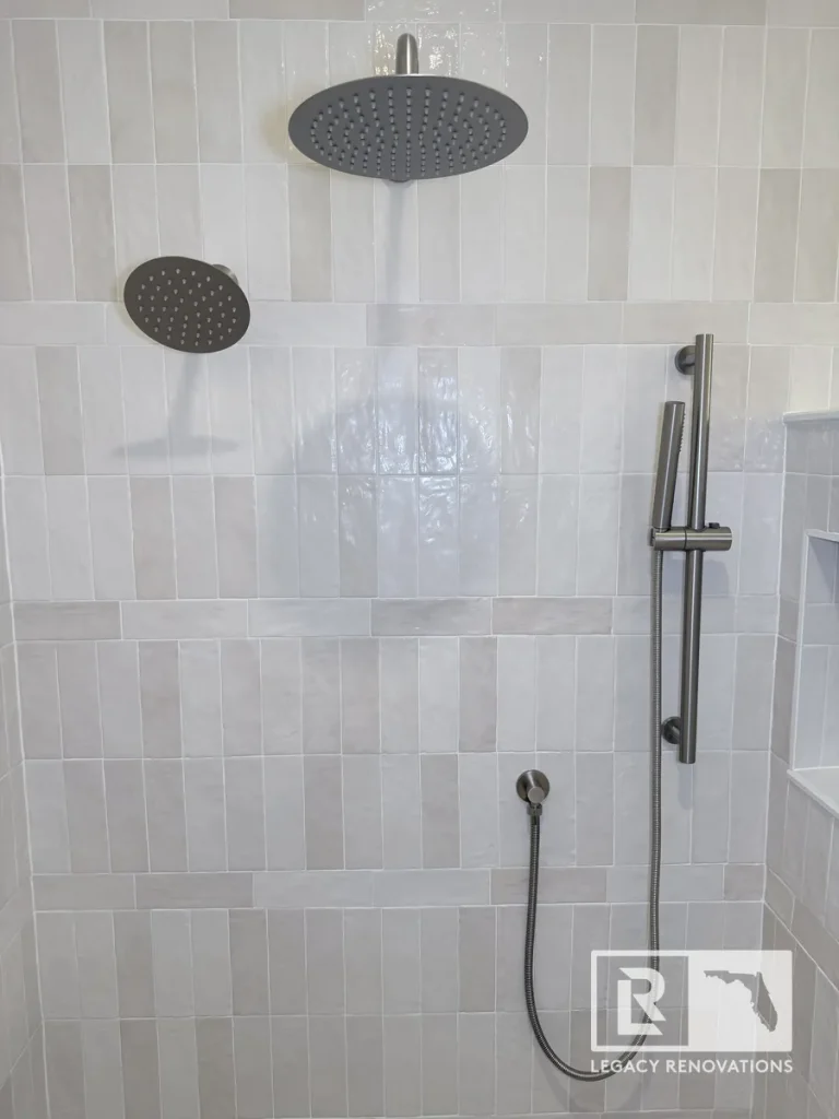 Full view of a brushed nickel rain shower head, side nozzle, and handheld wand mounted on off-white tile in Mandarin Jacksonville FL.