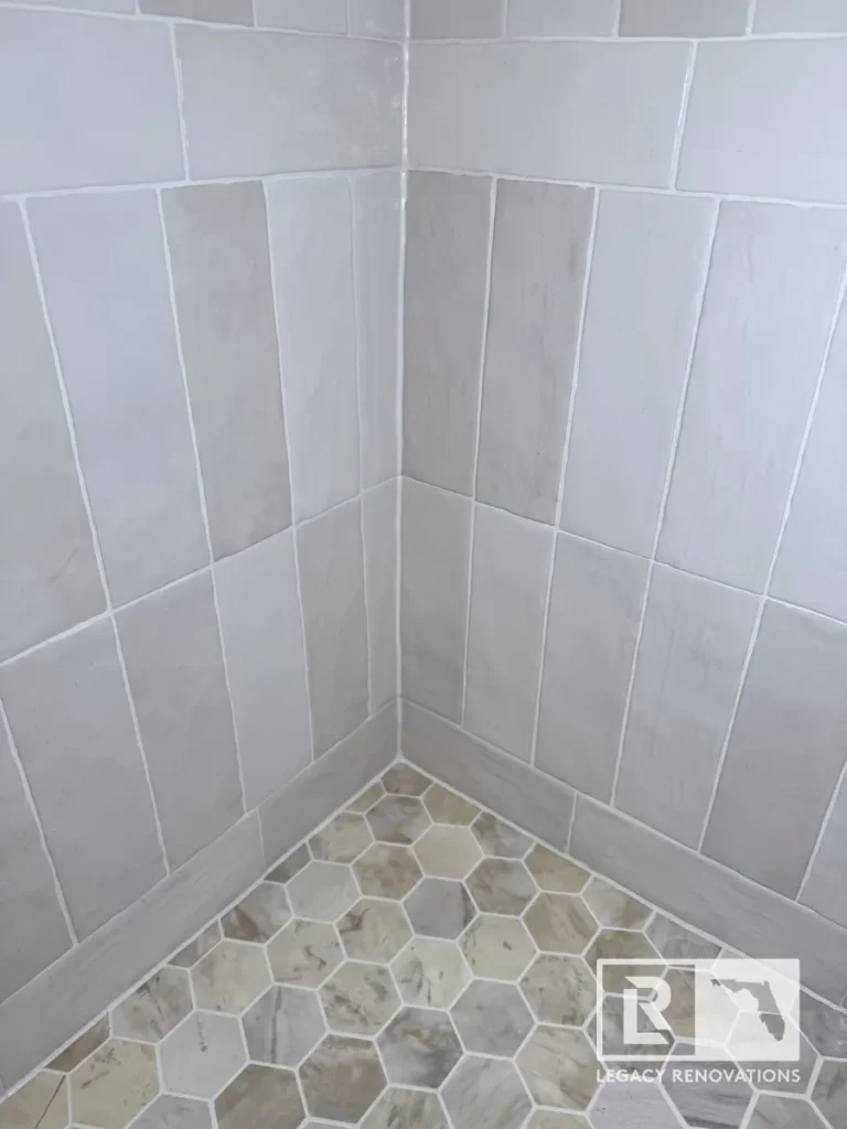 Bottom corner of a shower featuring hexagonal stone floor tiles meeting light gray vertical wall tiles in a Mandarin Jacksonville FL residence.