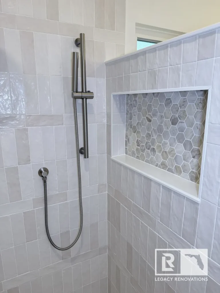 Recessed shower niche with gray hexagon marble tiles beside a slide-bar shower sprayer in a Mandarin Jacksonville FL bathroom.