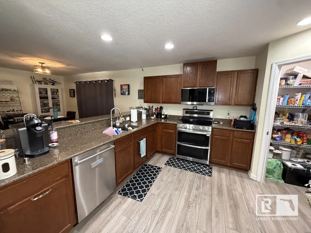 Wide-angle view of a Jacksonville FL home kitchen showing dark wood cabinets, granite island counter, stainless dishwasher, and stove.